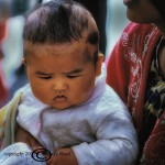 Uigar infant resembling the Happy Buddha sits in his mother's lap