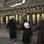 Three Tibetans spin prayer wheels before entering the Monastery