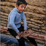 A young boy polishes a wooden utensil at his father's workshop